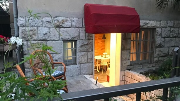Um edifício de pedra com toldo vermelho, uma cadeira de vime e uma mesa com flores brancas.
