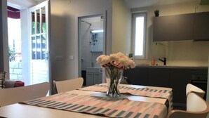 Uma sala de jantar com mesa posta para dois, um vaso de flores e vista para a cozinha e banheiro ao fundo.