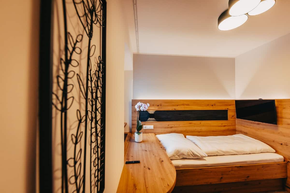Una cama de madera con cabecera, una mesita de noche y un pequeño florero blanco con flores.