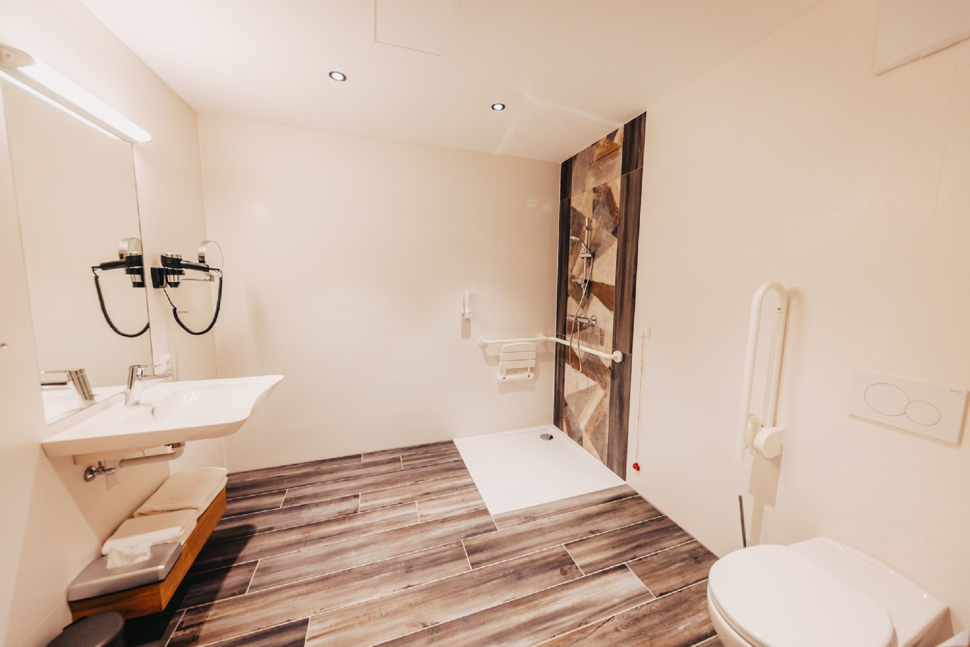 A modern bathroom with a wooden floor, a white sink, a toilet, and a shower area.