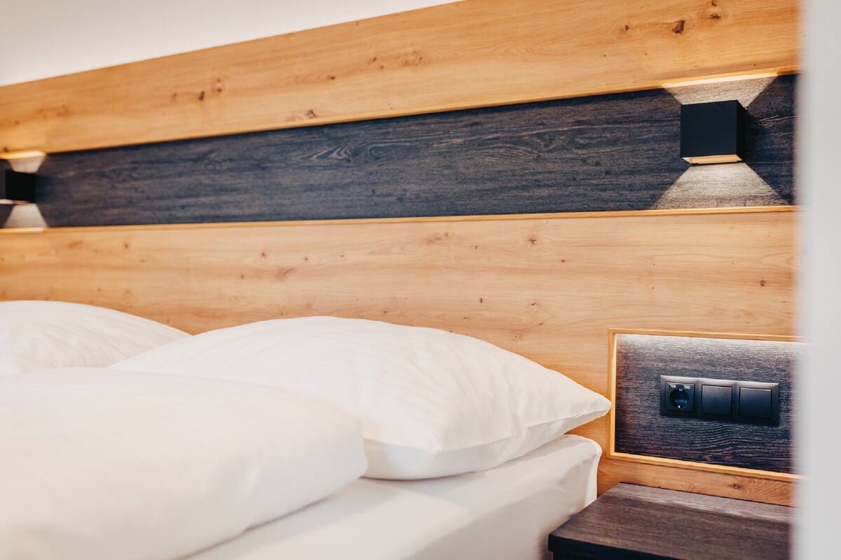 Cabecera de madera con panel oscuro y mesita de noche con toma de corriente.