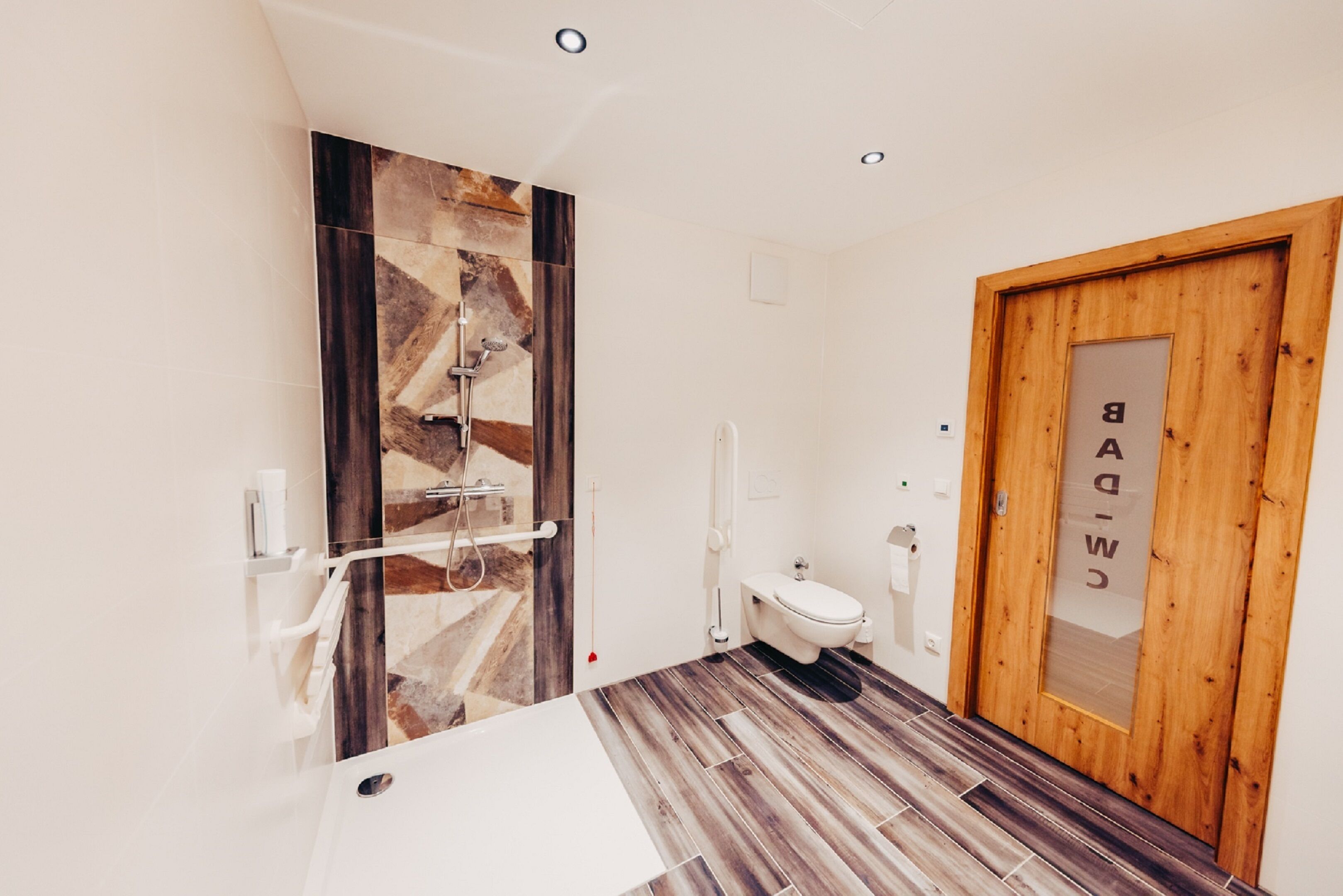 Uma casa de banho moderna com porta de madeira, pia branca e zona de duche.