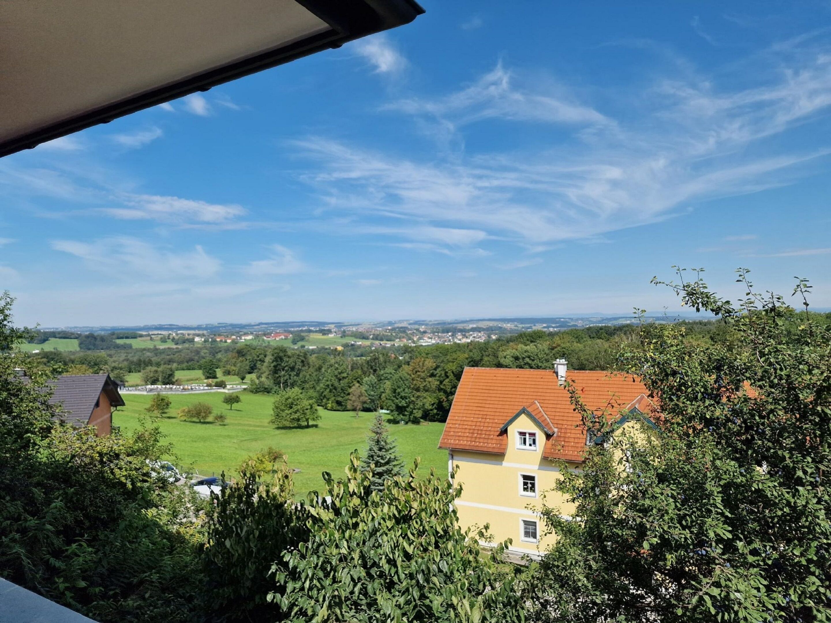 A view from a window overlooking a rural landscape with a yellow house and green fields.