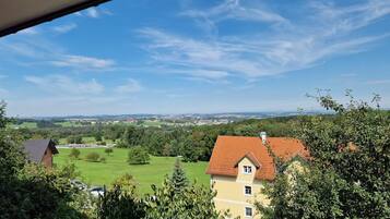 A view from a window overlooking a rural landscape with a yellow house and green fields.