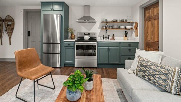 Una cocina moderna con gabinetes color turquesa, electrodomésticos de acero inoxidable y una mesa de comedor de madera con plantas.