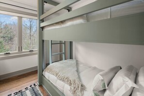 A bunk bed with a view of trees through a window.