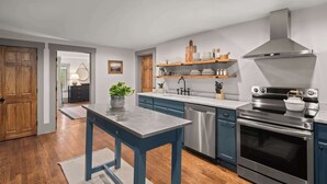 A modern kitchen with a wooden floor, a marble countertop, and stainless steel appliances. - 4BR Vermont Condo | Stowe Mountain & River Access (Stowe)