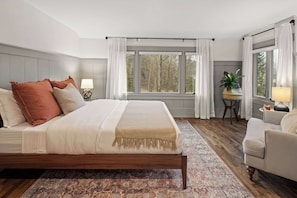 A bedroom with a wooden bed, a patterned rug, a desk with a lamp, and a view of trees through the window. - 4BR Vermont Condo | Stowe Mountain & River Access (Stowe)