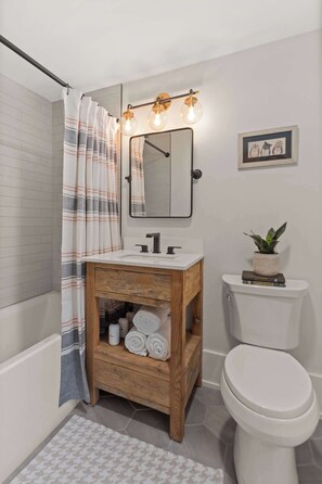 A modern bathroom with a wooden vanity, white toilet, and a shower curtain. - 4BR Vermont Condo | Stowe Mountain & River Access (Stowe)
