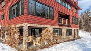A multi-story building with a stone foundation, large windows, and a balcony. - 4BR Vermont Condo | Stowe Mountain & River Access (Stowe)