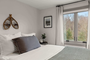 A bedroom with a bed, pillows, a bedside table with a plant and clock, a framed picture, and a window with curtains. - Cozy Vermont Escape | Stowe Mountain & Ski Resort (Stowe)