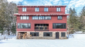 A two-story building with a stone foundation, large windows, and a balcony. - Vermont 2BR | Stowe Slopes & Swimming Holes (Stowe)