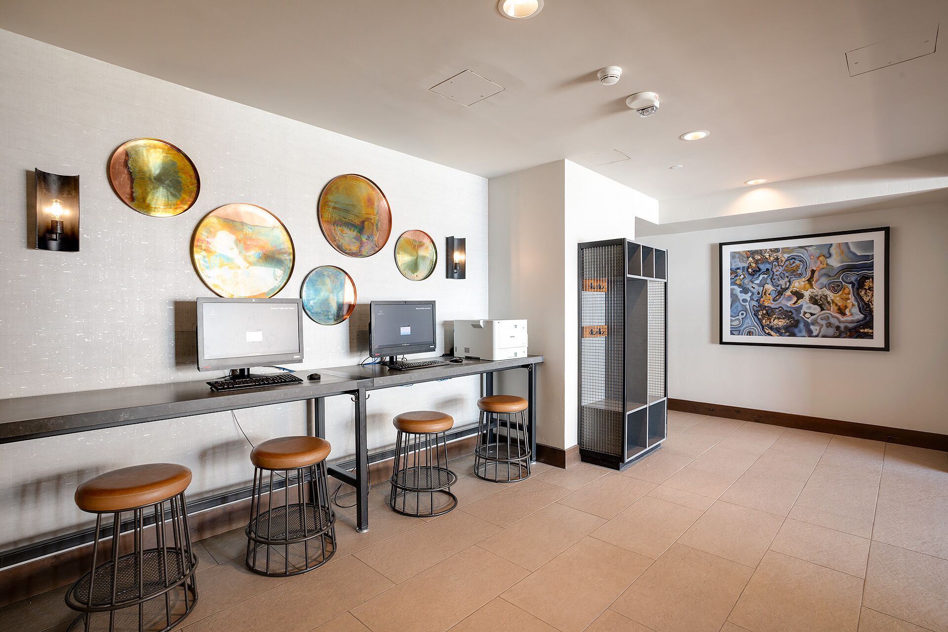 A modern kitchen with bar stools, a countertop with two computers, and decorative plates on the wall.