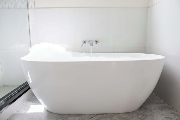 Une baignoire moderne, autoportante, dans une salle de bain dont les murs et le sol sont recouverts de carrelage.