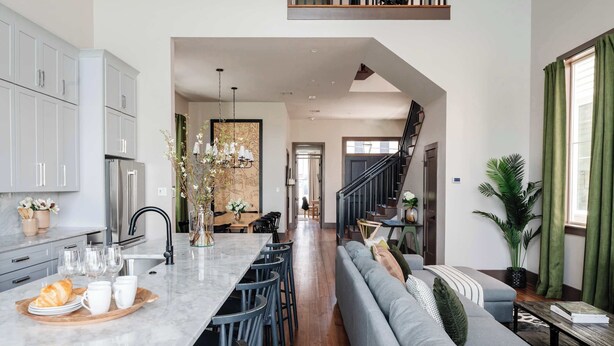 Una cocina moderna con armarios grises, encimera de mármol y un comedor con sofá gris y mesa de madera.