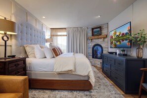 Een slaapkamer met een groot bed, een open haard, een televisie en een bureau.
