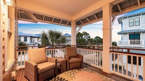 A covered porch with wicker furniture and a patterned rug, overlooking a residential area with houses and a clear sky. - Bay Views with Pool and Gym Access (Port St. Joe)