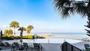 An infinity pool with lounge chairs, palm trees, and a view of the ocean. - Bay Views with Pool and Gym Access (Port St. Joe)
