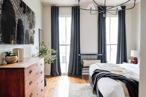 Ein Schlafzimmer mit Bett, Schminktisch und einem großen Fenster mit Vorhängen.