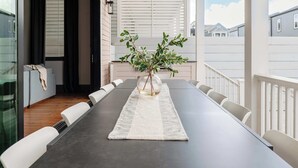 A dining area with a long table, white chairs, a vase with greenery, and a view of neighboring houses. - The 1300 | 7 Bedroom Luxe Home, Heated Pool & Spa (New Orleans)