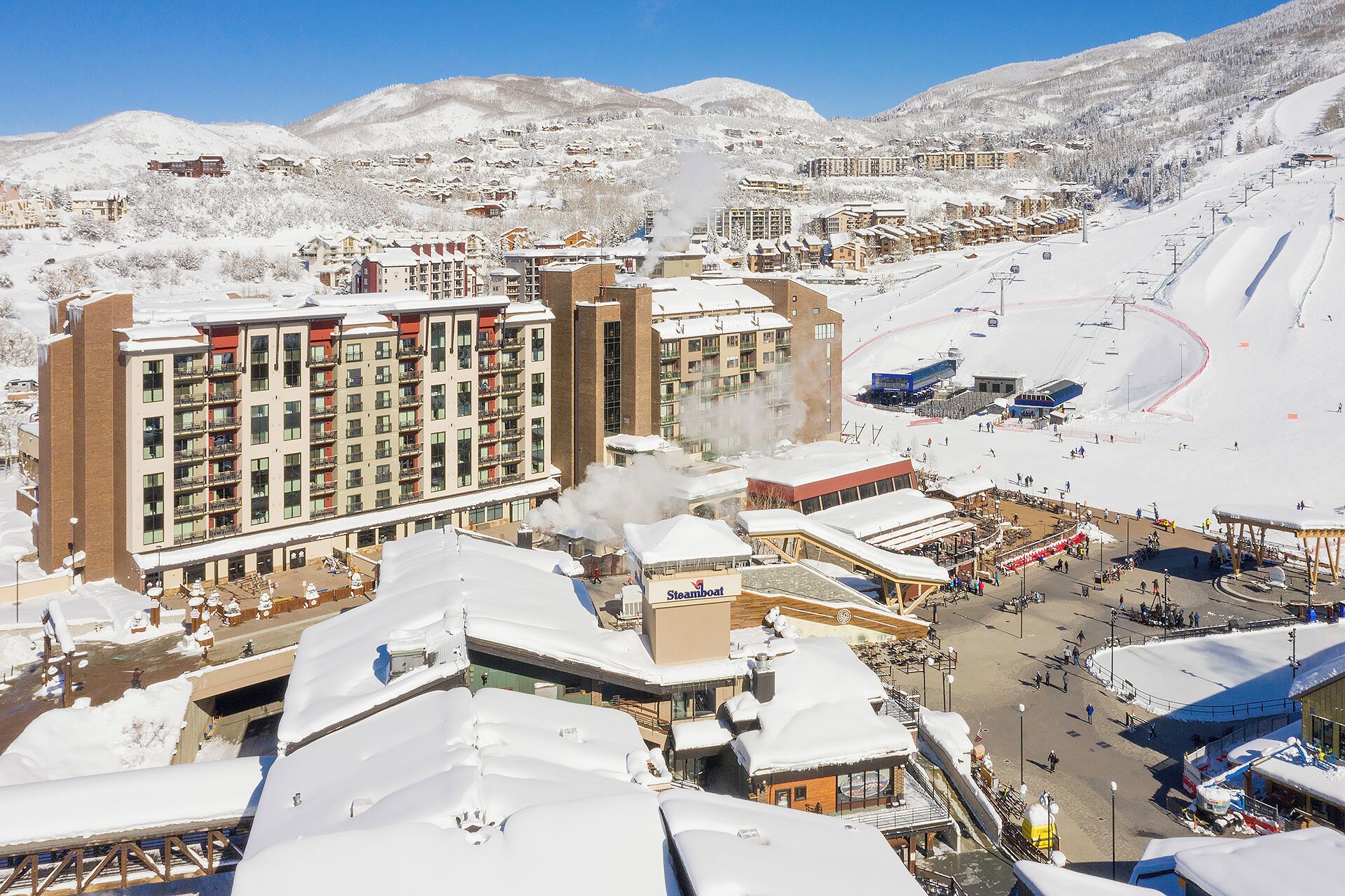 A snow-covered resort with multi-story buildings, a ski lift, and a snowmobile rental area.