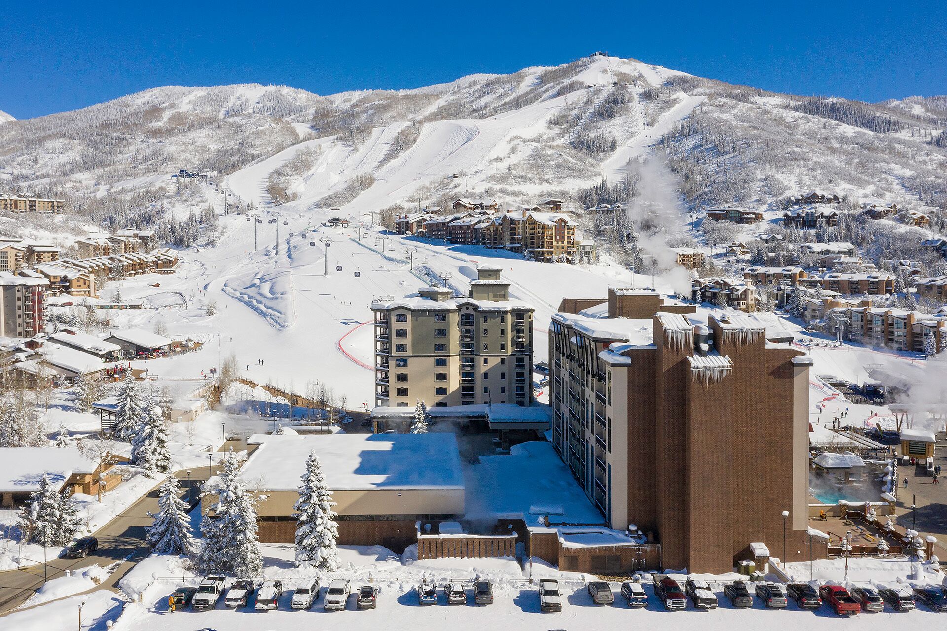 A ski resort with multiple buildings, a ski lift, and a parking area covered in snow.
