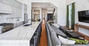 A modern kitchen with a marble countertop, stainless steel appliances, and a central island with bar stools. - The 1300 | Designer 6-bedroom, Close to Parades (New Orleans)