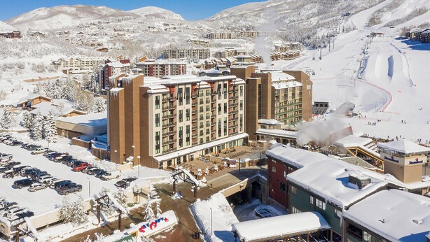 Un grand hôtel à plusieurs étages, avec un parking et une piste de ski en arrière-plan.