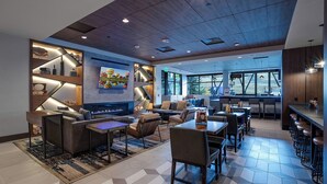 Un hall d’hôtel moderne doté d’une cheminée, de sièges confortables, d’un bar et de grandes fenêtres offrant une vue sur l’extérieur.