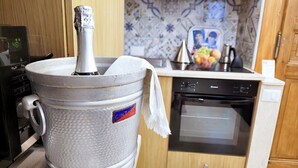 Keittiössä on suuri metallinen astia, liesi, uuni ja laatoitettu seinäosa työtason yläpuolella.