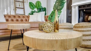 Una mesa de centro redonda de madera con superficie texturizada, un cuenco decorativo dorado y una planta verde en un florero dorado.