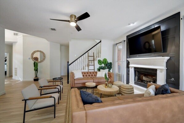A modern living room with a fireplace, leather sofas, a TV, and a ceiling fan.