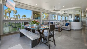 A spacious living area with a dining table, seating, and large windows offering a view of palm trees.