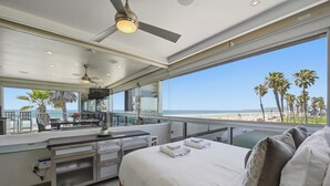 A modern hotel room with a balcony, a bed, a desk, and a view of the beach.