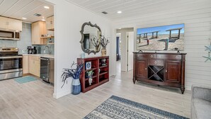 A spacious living area with a kitchen, wooden cabinets, a large mirror, and a television displaying a beach scene.