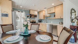 A modern kitchen with wooden cabinets, stainless steel appliances, and a dining area with a table set for four.