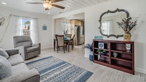 A spacious living room with a ceiling fan, a dining area with a table and chairs, and a kitchen in the background.