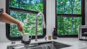 Una cocina moderna con un lavamanos de acero inoxidable, un grifo y una ventana con vistas a un bosque.