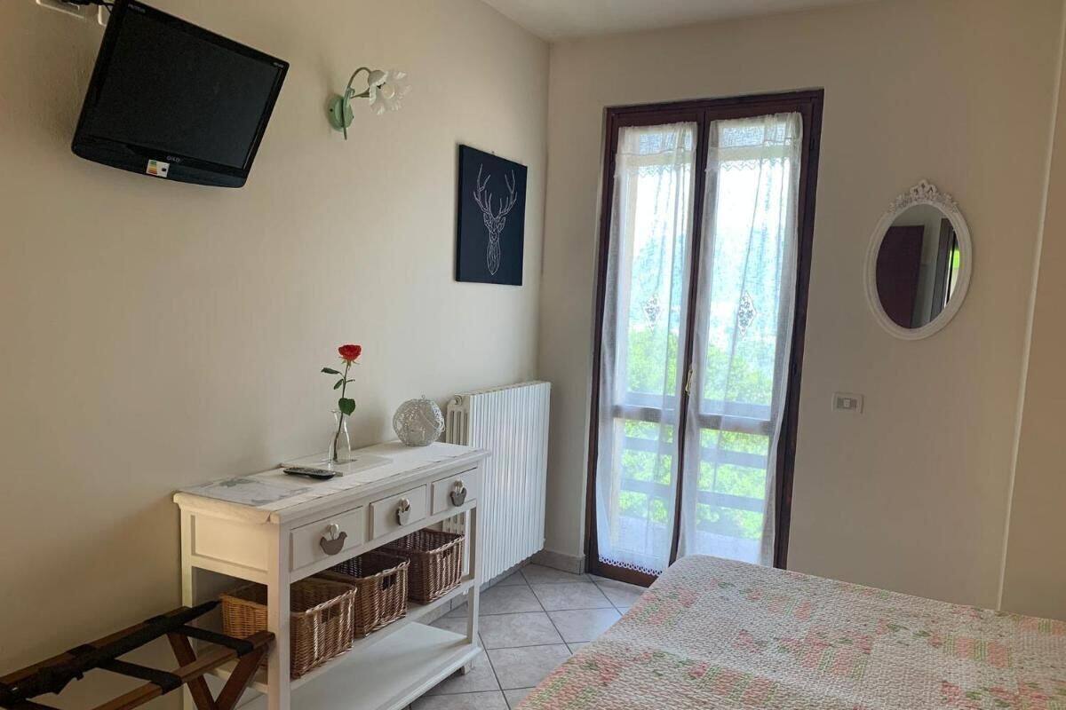 Ein Schlafzimmer mit Bett, Kommode, Fernseher, einem Fenster mit Vorhängen und einer Tür zu einem Außenbereich.