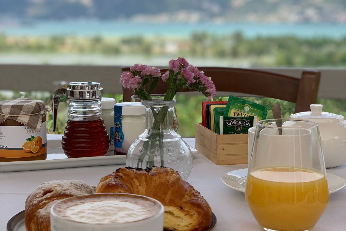 Ein Frühstückstisch mit Gebäck, einer Kaffeetasse, einem Orangensaftglas, einem Honigglas, einer Teedose und einer Vase mit Blumen.
