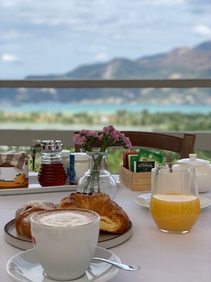 Una mesa de desayuno con pasteles, una taza de café, un vaso de zumo de naranja, un tarro de miel, una caja de té y un jarrón con flores.