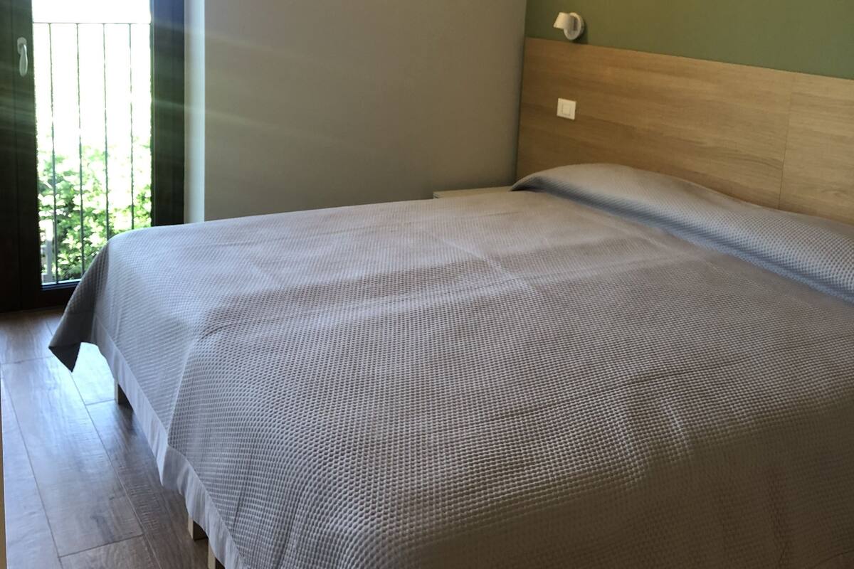 Ein Schlafzimmer mit einem Bett, einem Nachttisch, einer Wandleuchte und einer Tür, die auf einen Balkon führt.