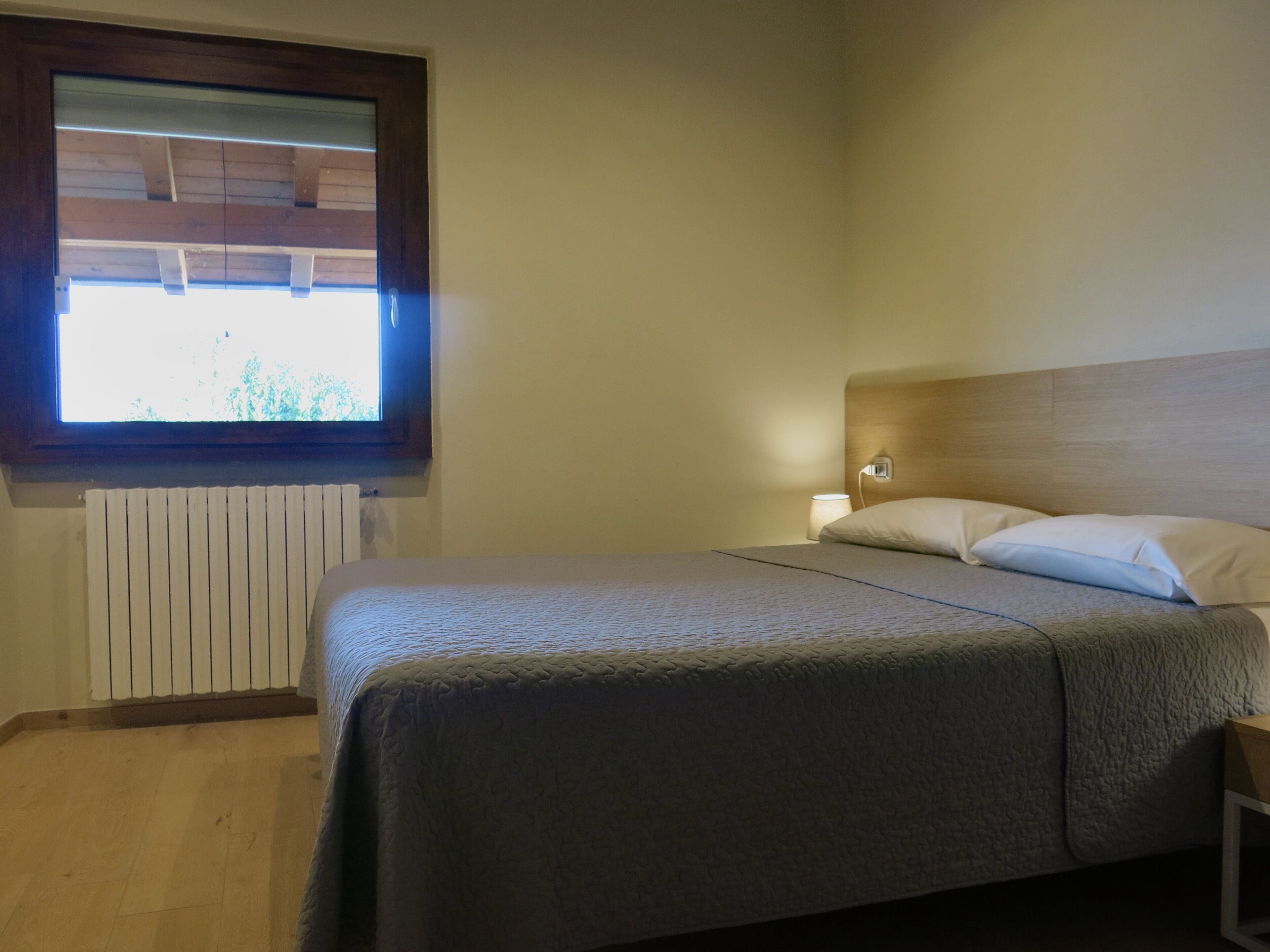 Un dormitorio con cama, ventana, radiador y mesita de noche.
