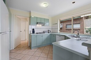 Kitchen features a stove, coffee maker, and tiled backsplash with a window offering a view.