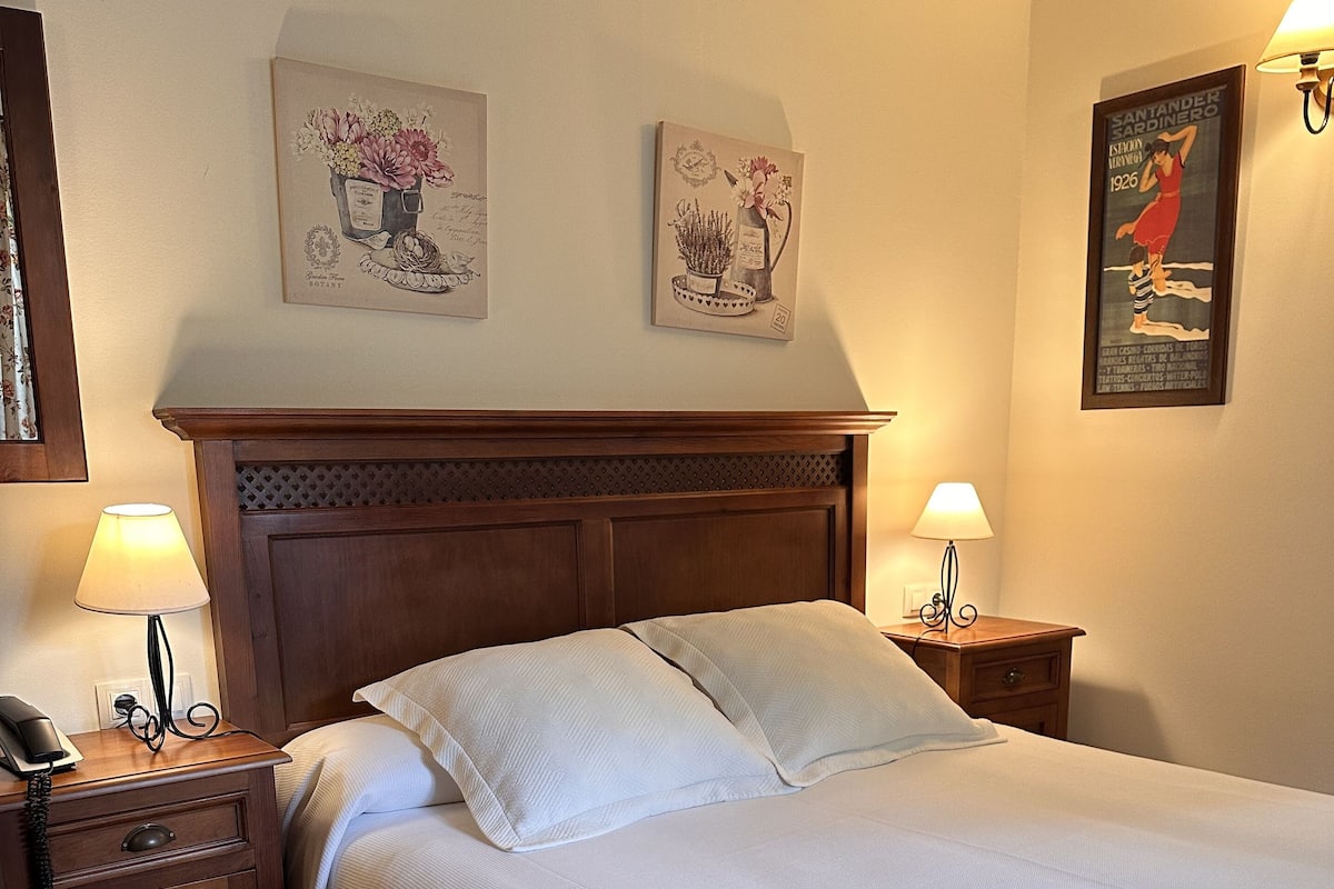 Una cama bien hecha con sábanas blancas, cabecera de madera y dos lámparas de noche.