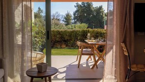 Ein Zimmer mit einer Schiebetür, die auf eine Terrasse im Freien führt. Die Terrasse hat einen Holztisch und Stühle, und auf einem kleinen runden Tisch steht ein Laptop.