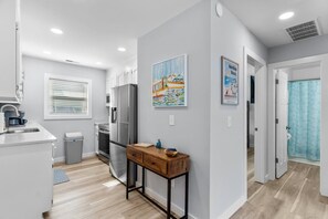 A modern kitchen with stainless steel appliances, a wooden side table, and artwork on the wall.
