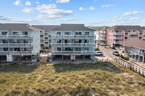 A beachfront hotel with multiple balconies, a parking area, and a grassy foreground.