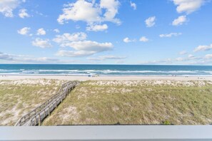 A beach with a wooden boardwalk leading to the shore, clear skies, and calm ocean waves.