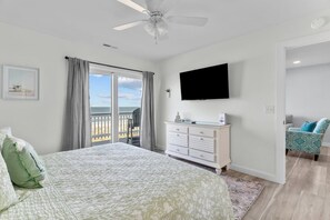 A bedroom with a bed, a dresser, a TV, and a balcony with a view.